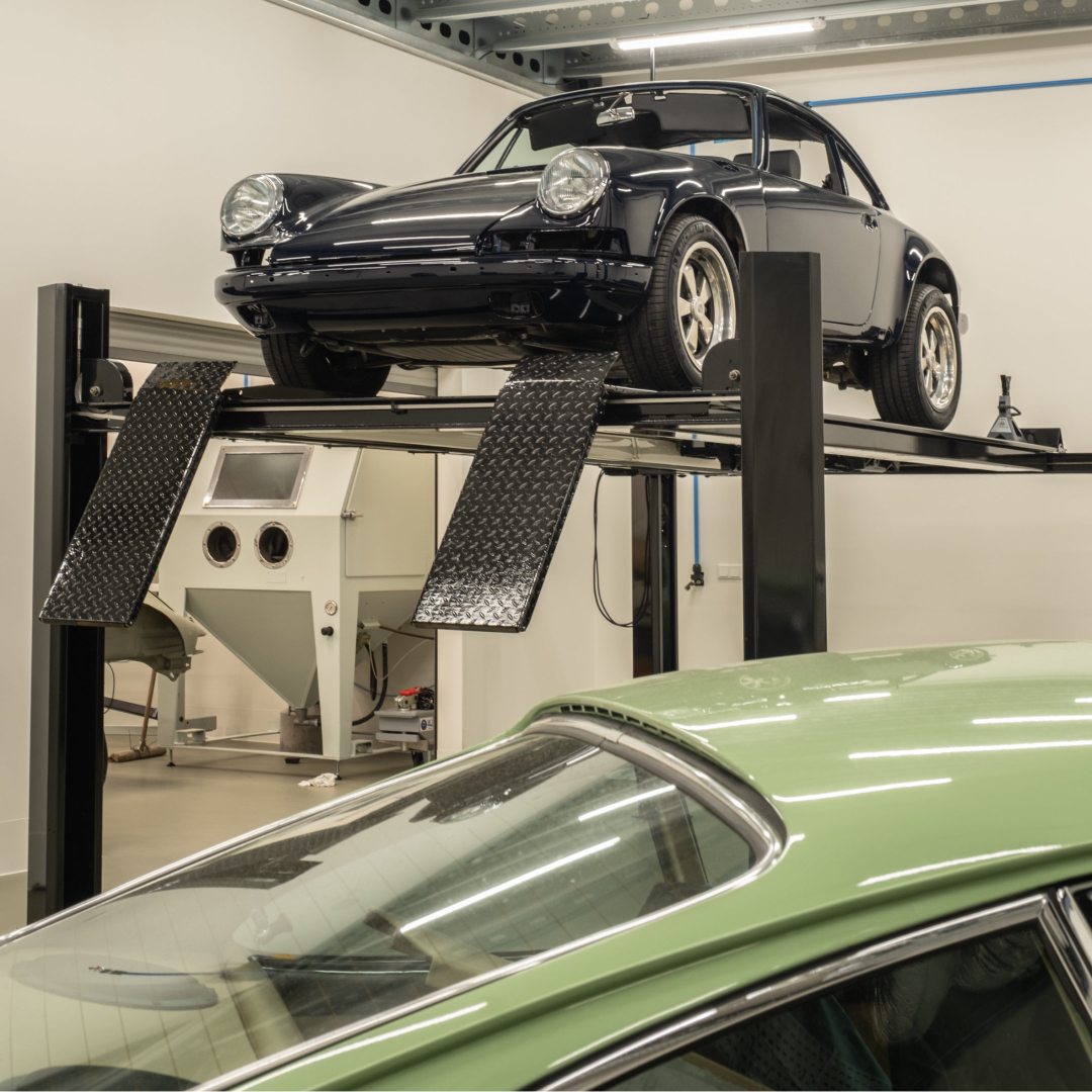 Green vehicle bodywork beside a raised chassis in the atelier
